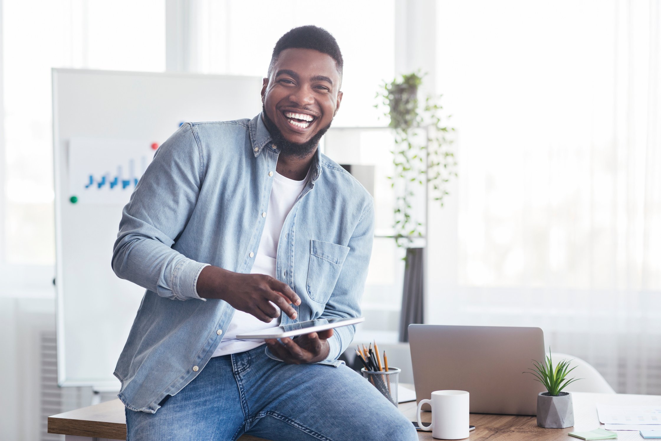 Cheerful black employee using digital tablet in office and laughing